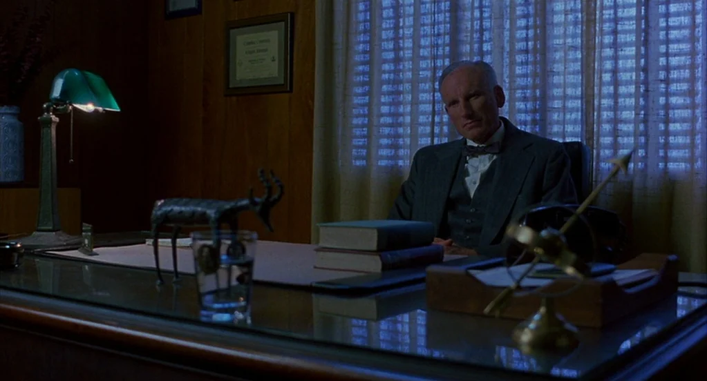 Far From Heaven (2002) movie still: medium — A wood-paneled office at night features a glass-topped desk with books and decorative ornaments. An…
