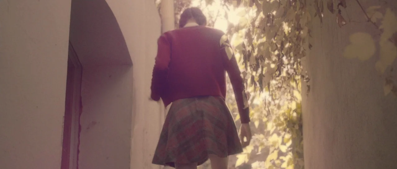Nymphomaniac Vol 1 (2013) movie still: medium — A narrow alleyway with light-colored walls and overhanging leaves illuminated by bright sunlight. A…