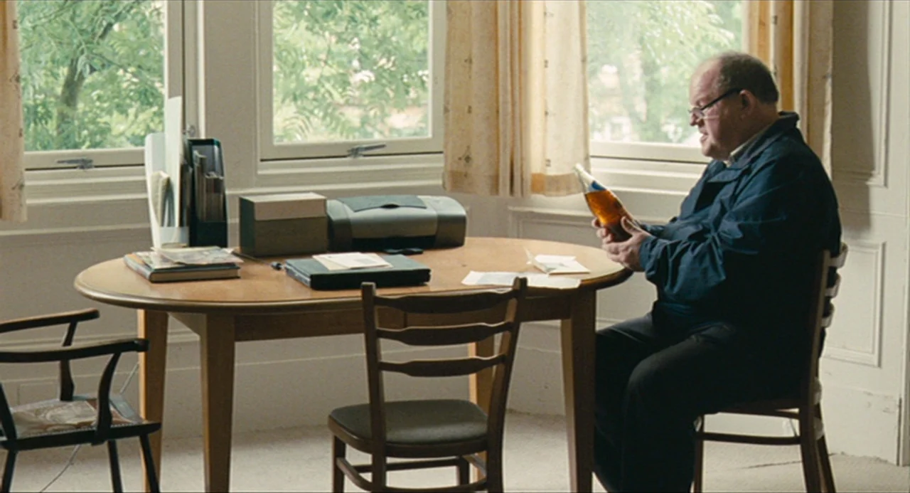 The Angel’s Share (2012) movie still: medium — A light-filled room features a wooden table, several chairs, and a large window. An elderly man in a…