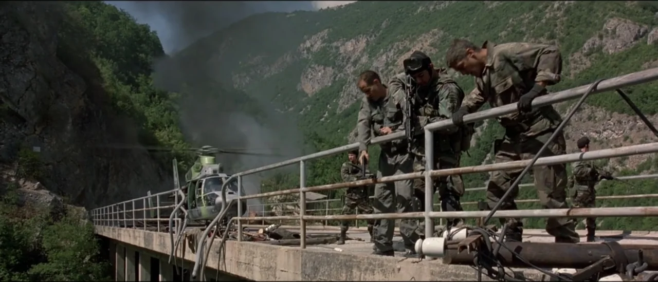 The Peacemaker (1997) movie still: wide — A group of soldiers stand on a concrete bridge overlooking a mountain valley. The men lean over the…