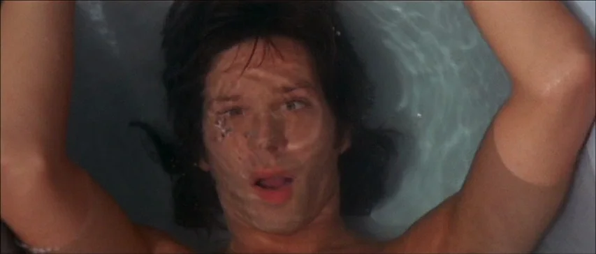 Four Flies On Grey Velvet (1971) movie still: closeup — A man's face is partially submerged in the water of a bathtub. He stares upward through the…