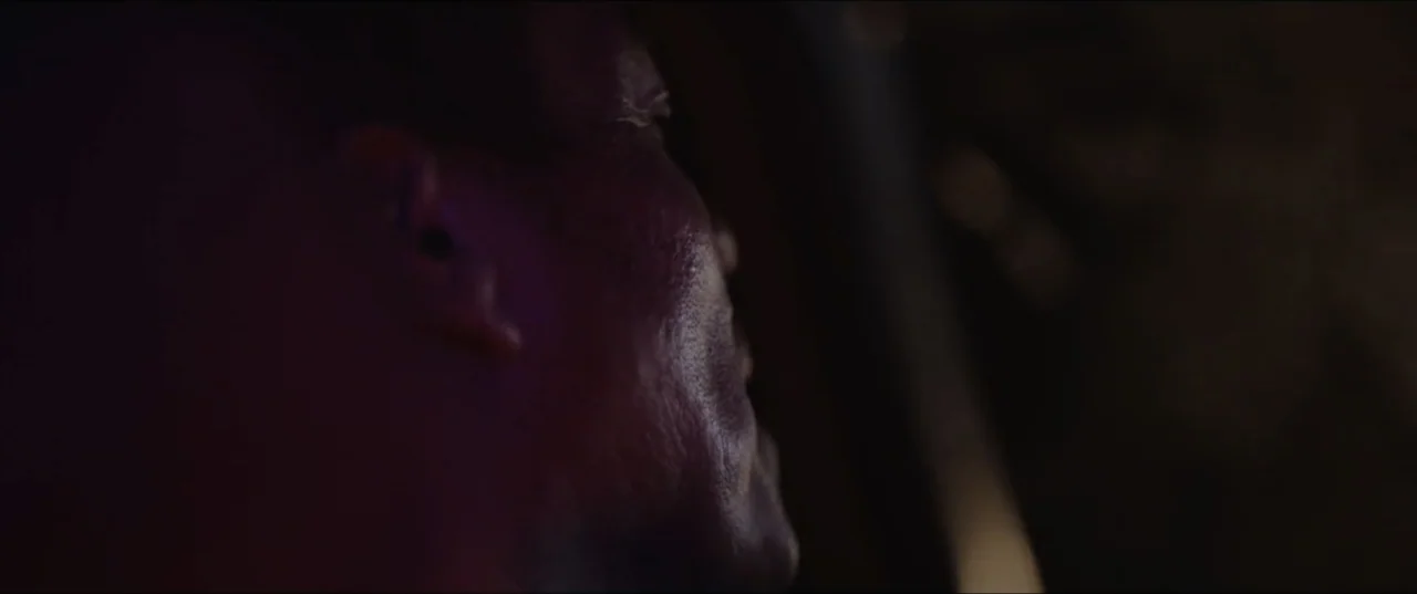 Death to Summer (2021) movie still: closeup — The interior of a vehicle at night is illuminated by dim, colored ambient light. A man sits in the…