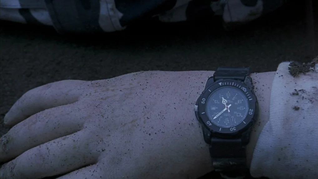 Mean Creek (2004) movie still: closeup — A person's hand covered in sand rests on a dark beach at night. A black wristwatch with a circular face is…