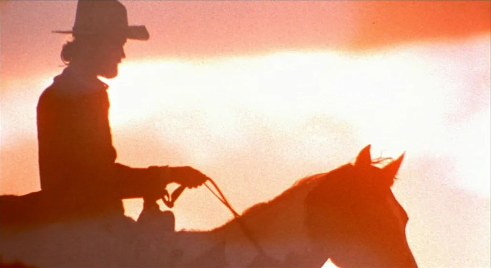 The Hired Hand (1971) movie still: medium — A vast, brightly lit orange sky serves as the backdrop for a rider. A man wearing a cowboy hat rides a…