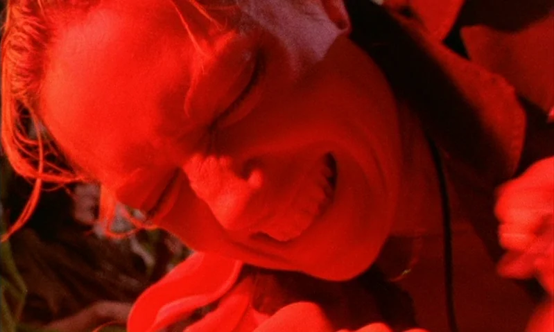Jubilee (1978) movie still: closeup — A close-up of a person's face bathed in intense red illumination. The subject has their eyes firmly shut while…