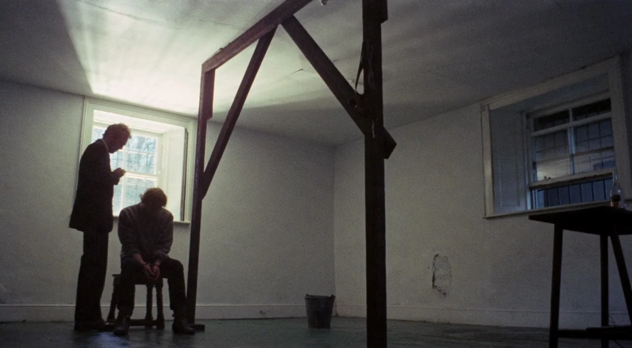 The Iguana with the Tongue of Fire (1971) movie still: wide — A sparsely furnished room with white walls and a large wooden gallows structure…