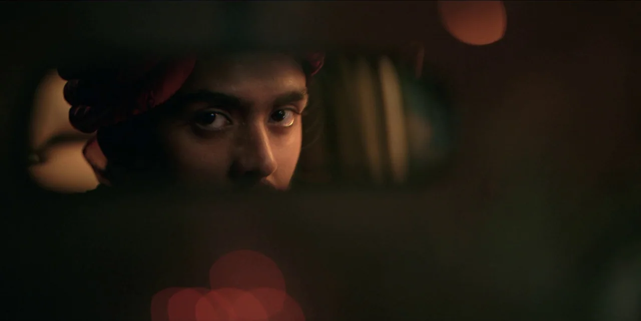 The White Tiger (2021) movie still: closeup — A dark vehicle interior with an out-of-focus bokeh background. A man looks directly into the rearview…