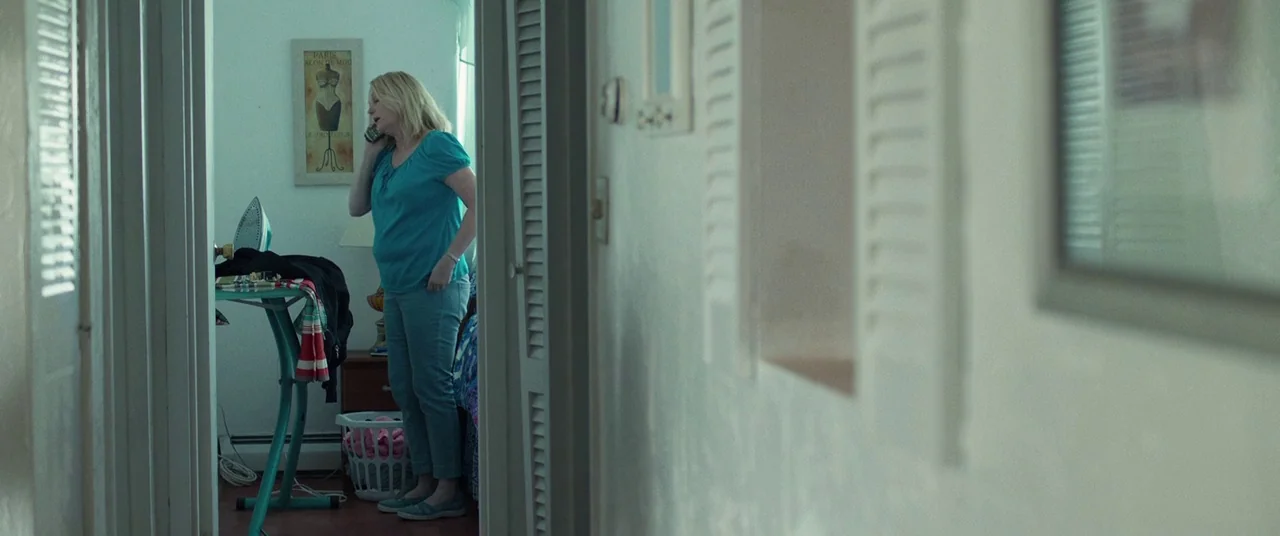 Stronger (2017) movie still: medium — A residential hallway with louvered doors leads into a room containing an ironing board. A woman stands in the…