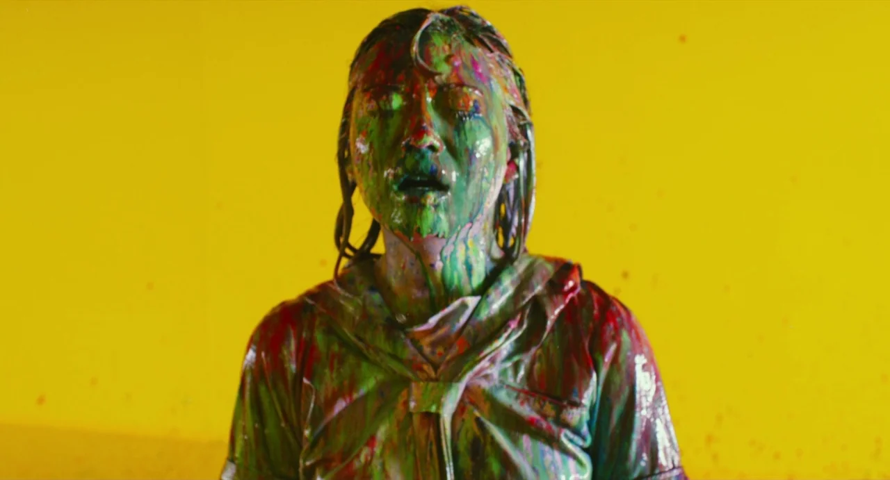 Making of: Antiporno (2016) movie still: medium — A person stands against a solid yellow backdrop in an indoor studio environment. The subject is…