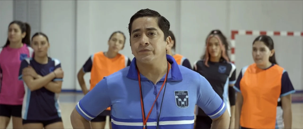 Disconnected 2 (2025) movie still: medium — A group of female students in athletic gear stands behind a coach in a gym. The coach faces forward…