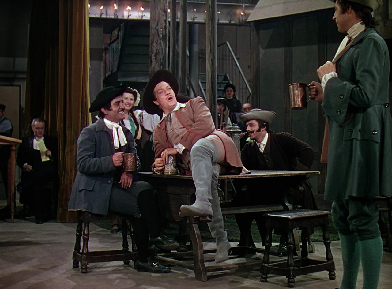 Phantom of the Opera (1943) movie still: fullbody — A theatrical tavern set features wooden tables, stools, and a small stage. Several men in period…