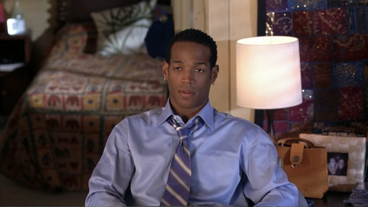 White Chicks (2004) movie still: medium — A furnished bedroom features a bed with a patterned quilt and a table lamp. A man sits in front of the…