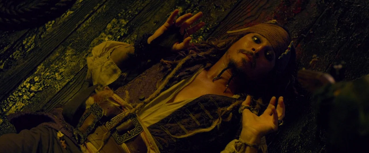 Pirates of the Caribbean: On Stranger Tides movie still: medium — A dark, worn wooden ship deck is lit by a harsh, single-source light. A man in…