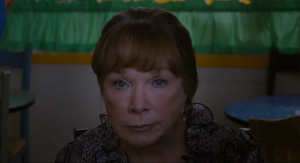 Bernie (2011) movie still: closeup — An interior view of a dining booth with a green curtain in the background. An elderly woman sits directly in…