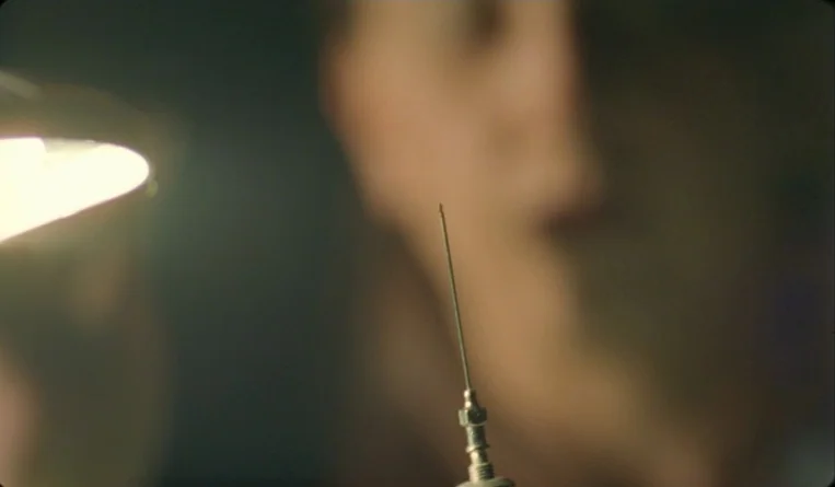 The Turn of the Century (2001) movie still: closeup — A close-up of a sharp metal needle tip held against a blurred dark background. The needle is…