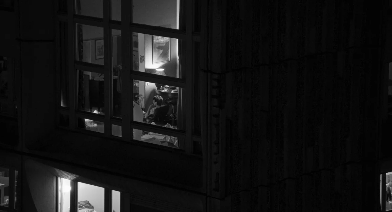 Paris, 13th District (2021) movie still: wide — A dark concrete apartment building exterior at night with one illuminated window visible. A lone…