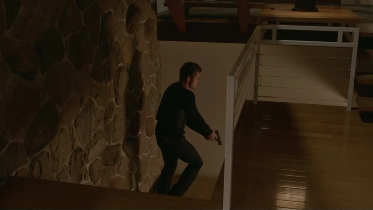 The Captive (2014) movie still: fullbody — A modern interior staircase features a rough-textured stone wall and wood flooring. A man descends the…
