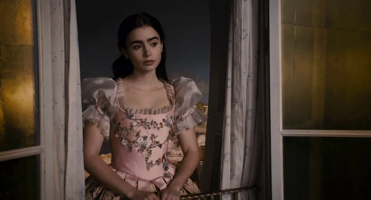 Mirror Mirror (2012) movie still: medium — A woman stands between open glass panels overlooking a dark, stylized night landscape. She gazes outward…