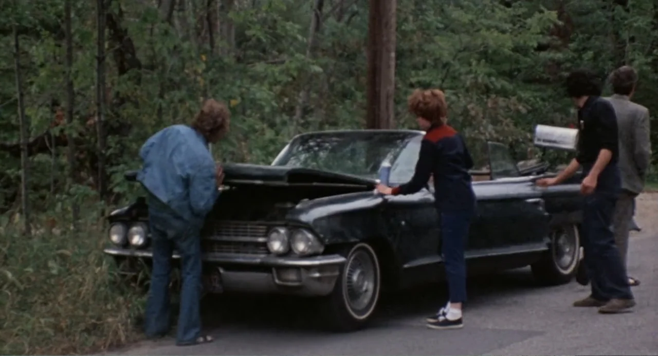 The Last House on the Left (2009) movie still: fullbody — A group of four young adults gather around a broken-down car on a roadside. The dark…