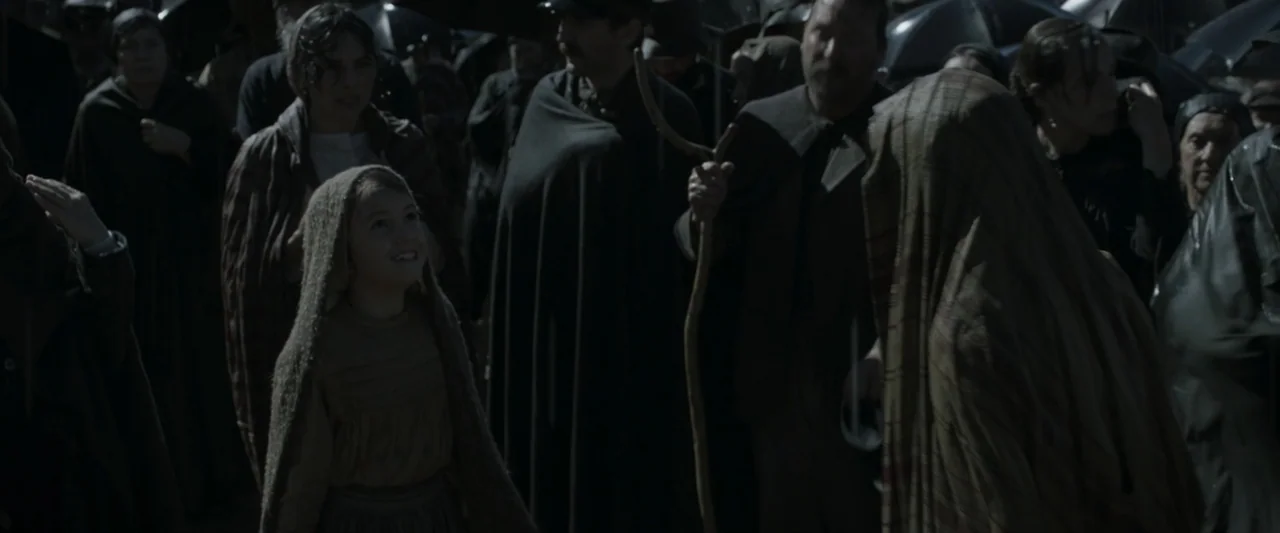Fatima (2020) movie still: medium — A dense crowd of people in period-appropriate attire stands close together under dark umbrellas. A young girl in…