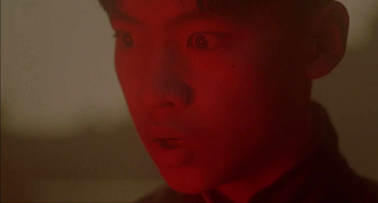 Shanghai Triad (1995) movie still: closeup — The frame shows a dark interior illuminated entirely by a single deep red light source. A young East…