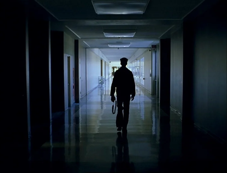 Elephant (2003) movie still: fullbody — A long, symmetrical school hallway with high-gloss floors and fluorescent light fixtures overhead. A lone…