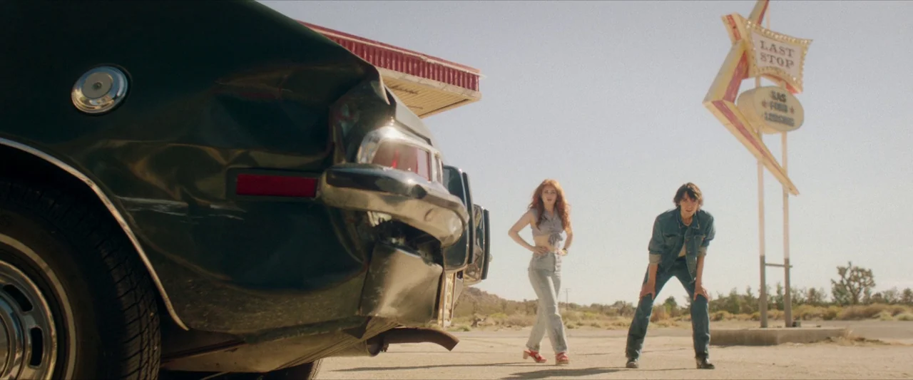 The Last Stop in Yuma County (2023) movie still: wide — A desolate desert gas station under a clear, bright sky features a vintage sign. A woman…