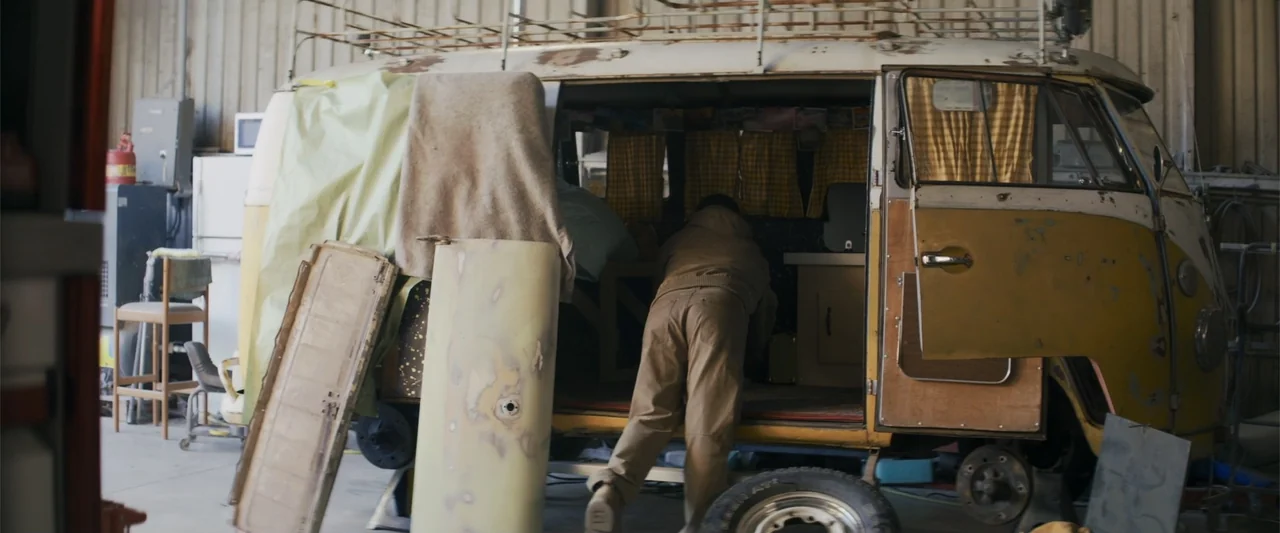 Holiday Harmony (2022) movie still: medium — A cluttered workshop contains a vintage van under repair with a detached door leaning nearby. A person…