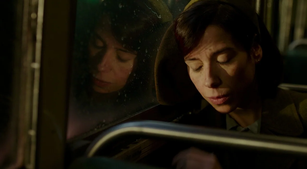 The Shape of Water (2017) movie still: closeup — A woman sits next to a rain-covered window on a dark transit vehicle. She leans her head against…