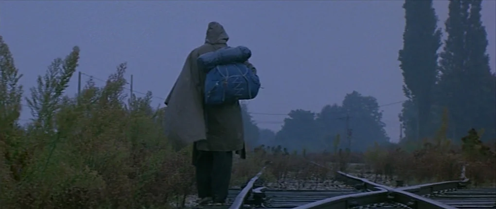 IP5 (1992) movie still: fullbody — A set of railway tracks stretches through an overgrown, misty landscape during early morning. A person wearing a…