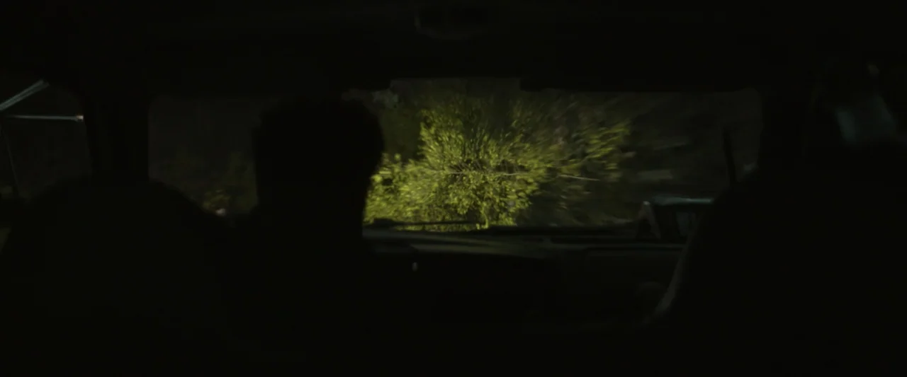 Wolf Man (2025) movie still: medium — The view from inside a car at night looking out the front windshield. The driver's silhouette is visible while…