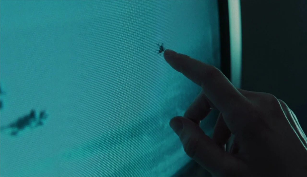 The Ring (2002) movie still: closeup — A human finger touches the surface of a glowing blue television screen. A small dark smudge or mark on the…
