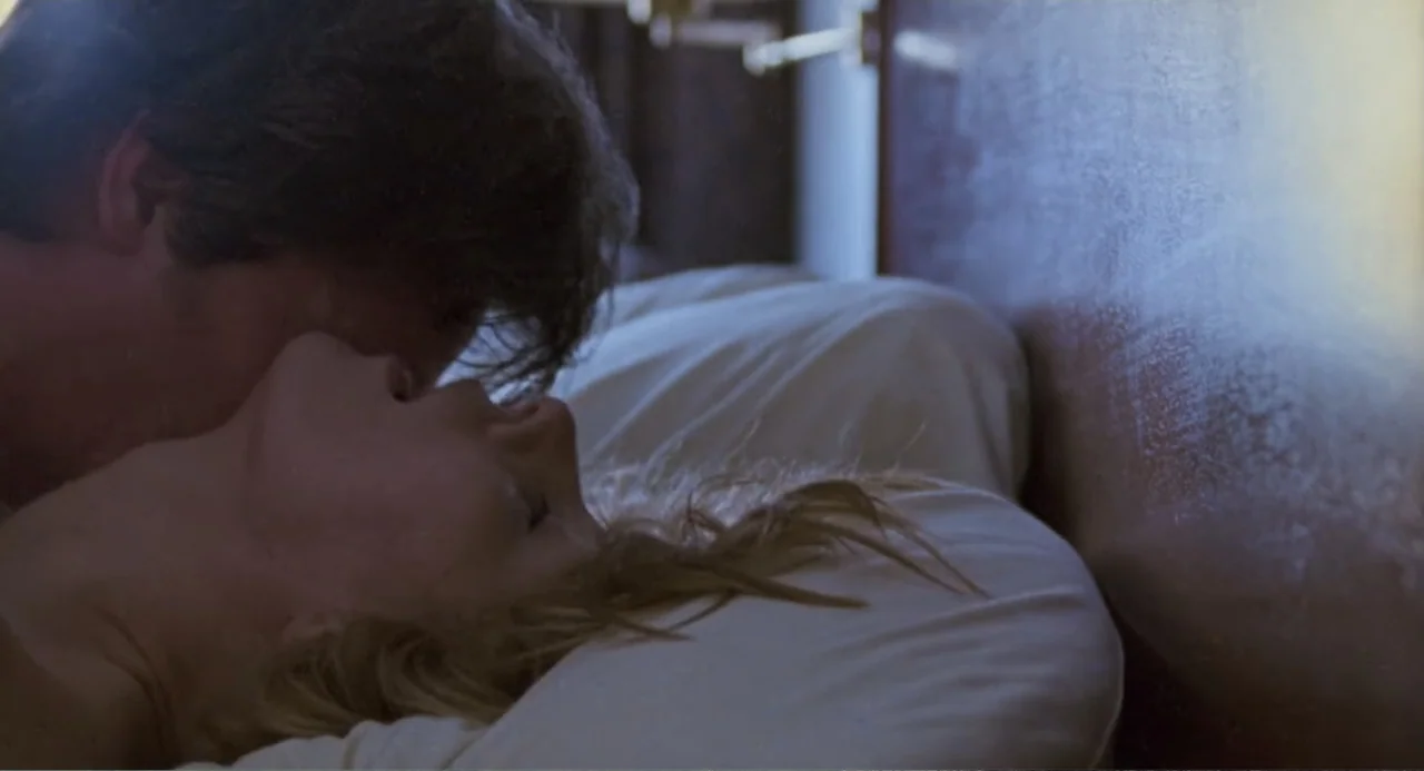 Forty Shades of Blue (2005) movie still: closeup — A modern bedroom features a wooden headboard and white pillows on a bed. A man and a woman lie…