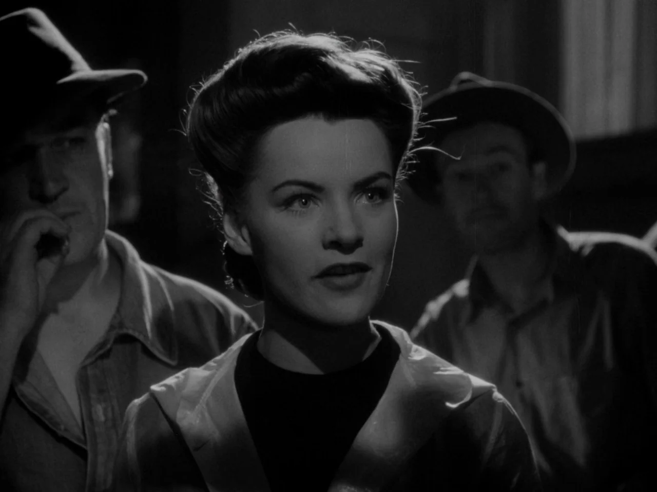 Phantom Lady (1944) movie still: medium — Three individuals stand closely together in a dimly lit room with high-contrast shadows. The woman in the…