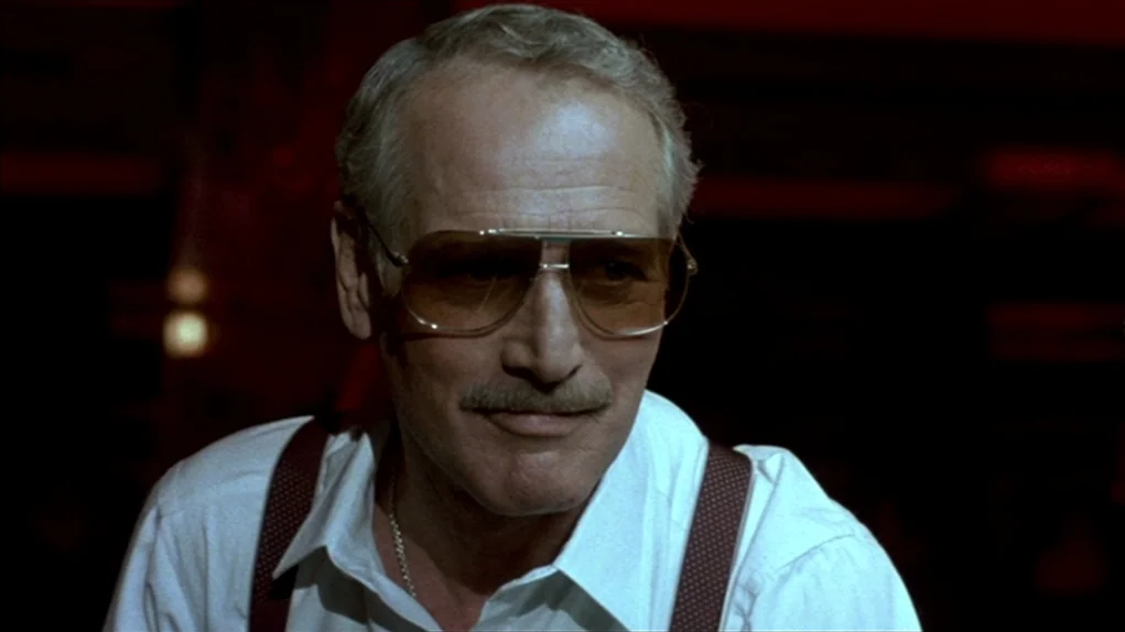 The Colour of Money (1986) movie still: closeup — A dark indoor space with minimal ambient lighting and deep, saturated red tones. An older man…