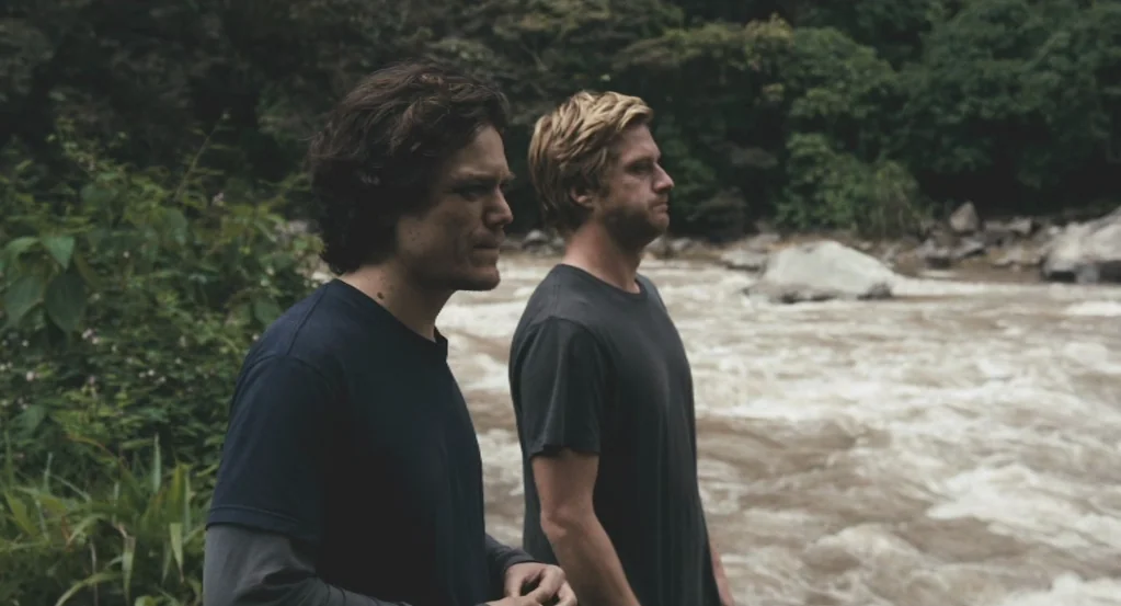 My Son, My Son, What Have Ye Done? (2009) movie still: medium — A riverbank with rushing brown water and dense green foliage in the background. Two…