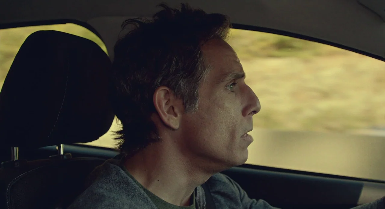 While We’re Young (2014) movie still: closeup — The interior of a moving car is shown with a blurry landscape passing outside. A man is driving and…