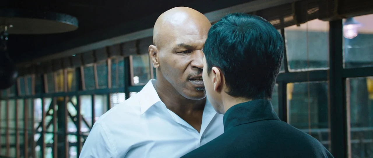 Ip Man 3 (2015) movie still: medium — A modern training gym features dark architectural framing and a blurred background. Two men stand in close…