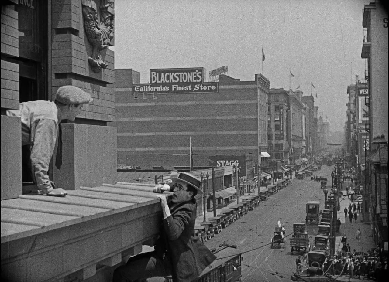 Safety Last! (1923) movie still: wide — A bustling 1920s downtown city street viewed from a high vantage point. A man clings precariously to the…
