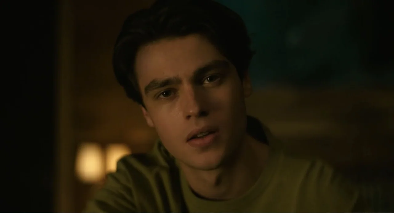 Turtles All the Way Down (2024) movie still: closeup — A dimly lit interior space with soft, warm light falling on the subject's face. A young man…