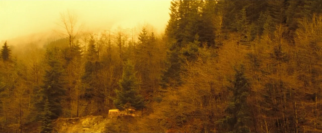 Trick ‘R Treat (2007) movie still: establishing — A dense coniferous forest covers a hillside under a thick, yellowish atmospheric haze. A small…