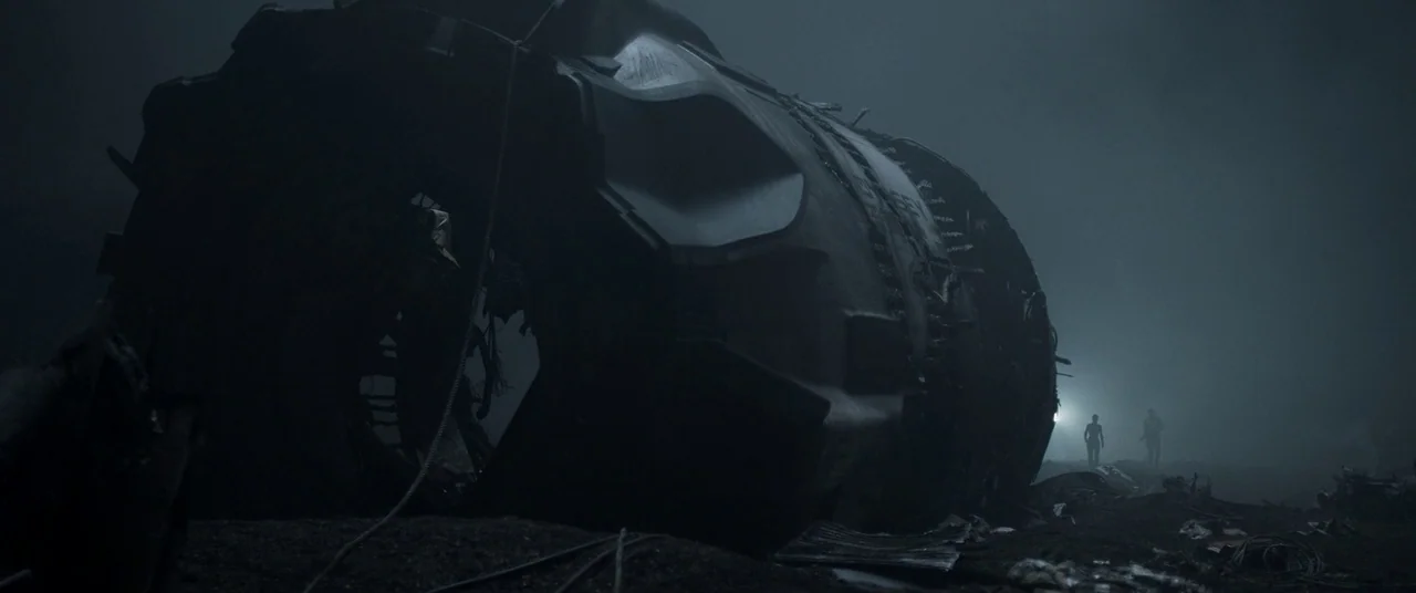 Oblivion (2013) movie still: wide — A massive, mangled aircraft turbine rests on a dark, barren, fog-filled landscape at night. Two small figures…