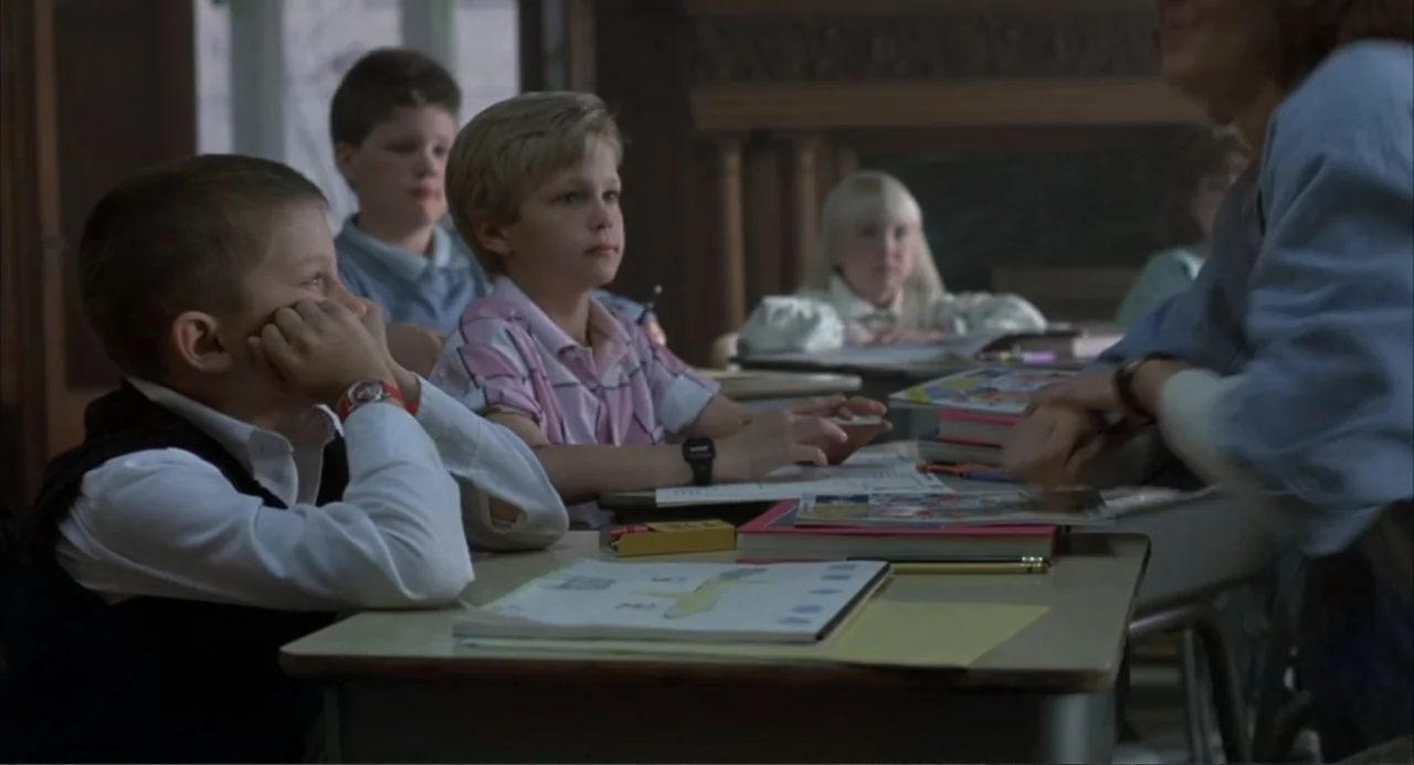 Poltergeist III (1988) movie still: medium — An elementary school classroom features rows of wooden desks and scattered student notebooks. Three…