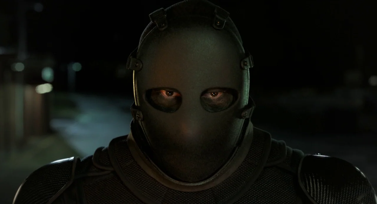 Gemini Man (2019) movie still: closeup — A night exterior on a dark city street shows a figure in black armor. The person wears a matte black…