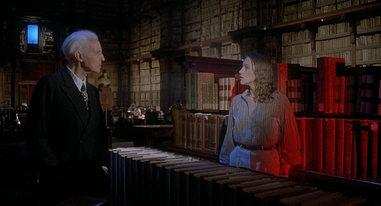 Inferno (1980) movie still: fullbody — A vast, dim, multi-story hall filled with floor-to-ceiling rows of old, leather-bound books. Two people stand…