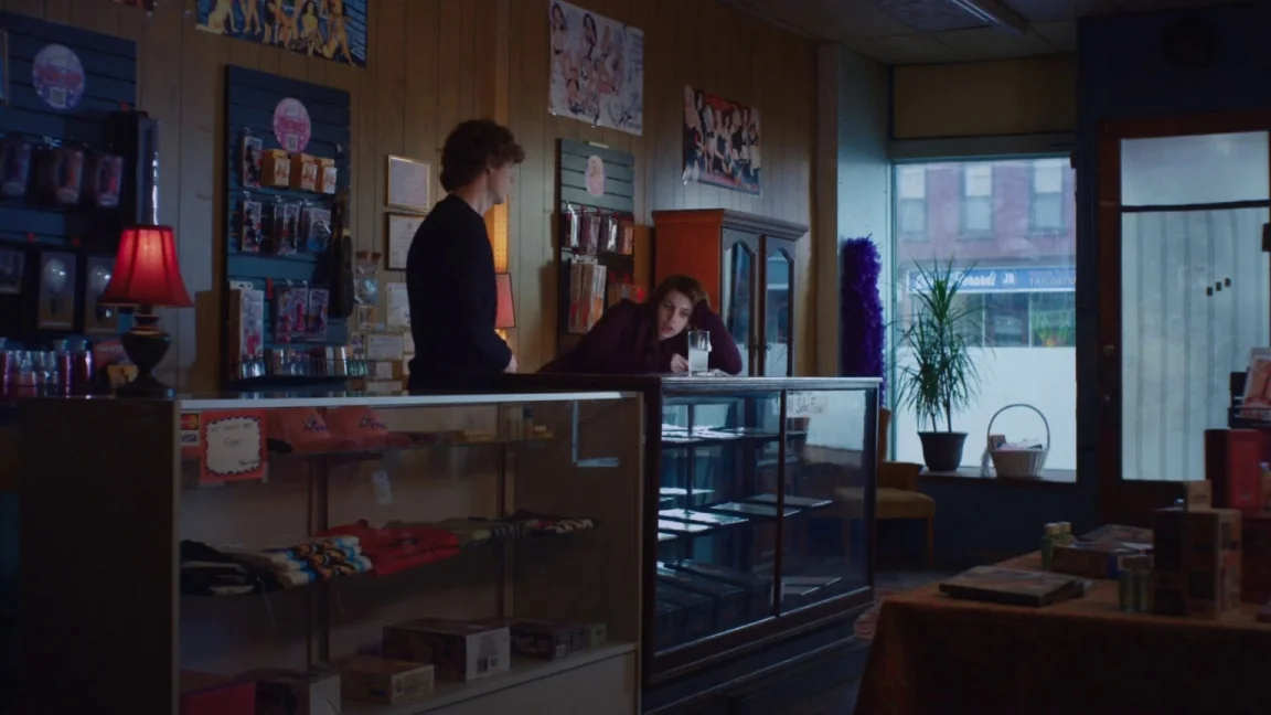 Adult World (2013) movie still: medium — A small retail shop with wood-paneled walls features glass display counters and merchandise shelves. A…