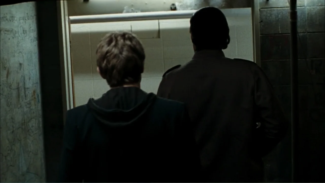 Driven to Kill (2009) movie still: medium — A dark, narrow corridor features graffiti-covered walls and a central open doorway. Two men walk through…