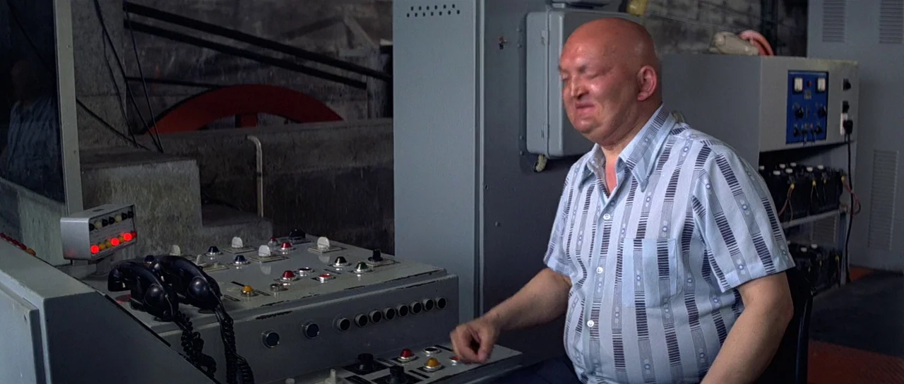 Moonraker (1979) movie still: medium — A utilitarian industrial space with large gray metal cabinets and switchgear components. A middle-aged man…
