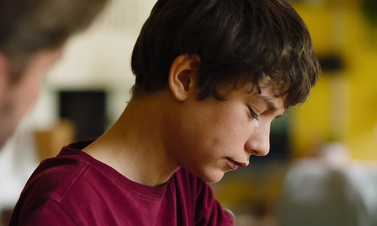 Close (2022) movie still: closeup — A close-up shot showing the profile of a teenager in a bright interior room. A single tear rolls down the cheek…
