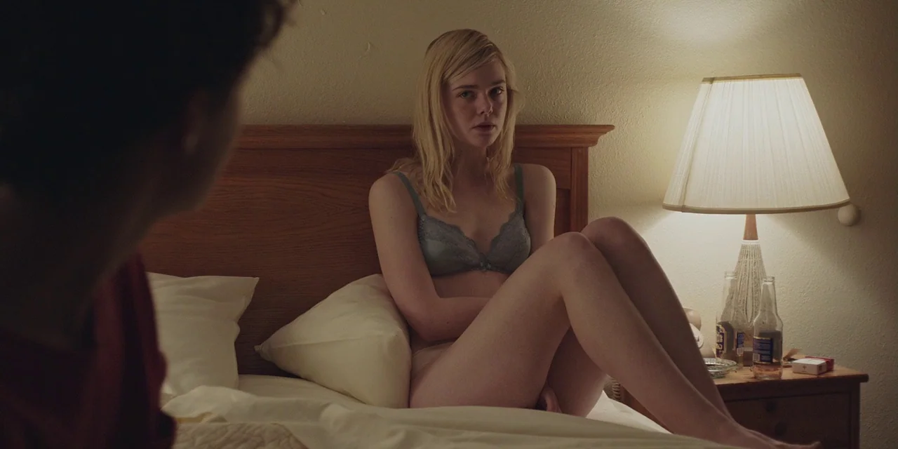 20th Century Women (2016) movie still: medium — A dimly lit motel room features a wooden headboard and a bedside lamp. A young woman sits on the…